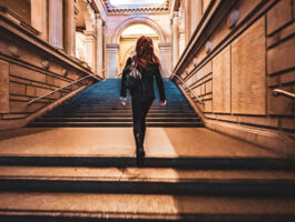 long haired woman runs up the grand stairs of the metropoltian museum of art