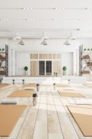 Bright sunny yoga studio with white walls blond wood floors orange mats in semetrical order