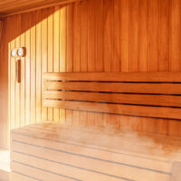 Cedar lined walls and bench system with steam inside a sauna, thermometer and hydrometer on the wall